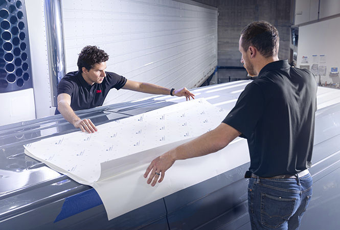 Technici die 3M Cooling Film aanbrengen op het dak van een voertuig in een servicewerkplaats.
